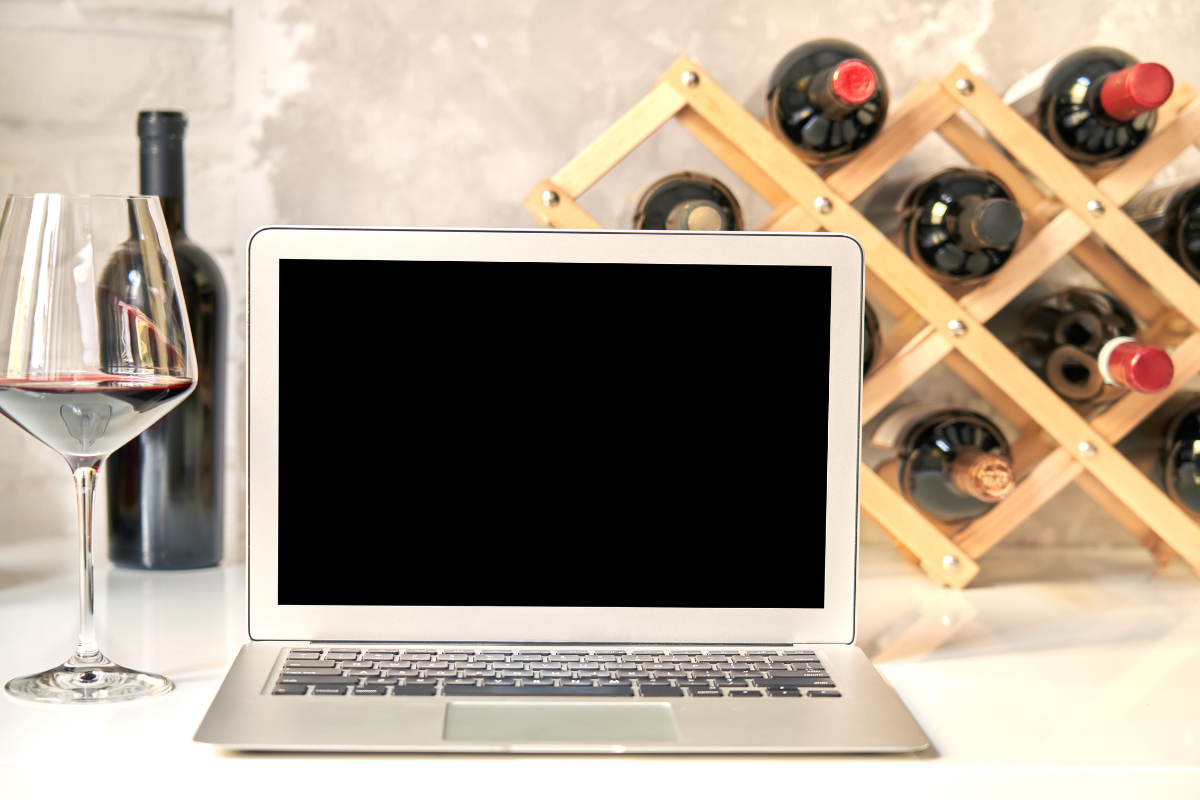 Un PC su una scrivania con un calice di vino rosso e delle bottiglie di vino
